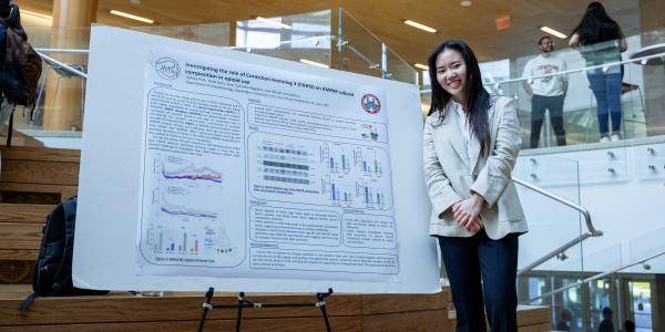 Young woman standing and smiling next to undergraduate research poster